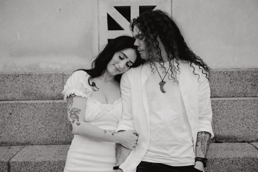 A black and white portrait of a couple leaning against a wall with a geometric pattern.