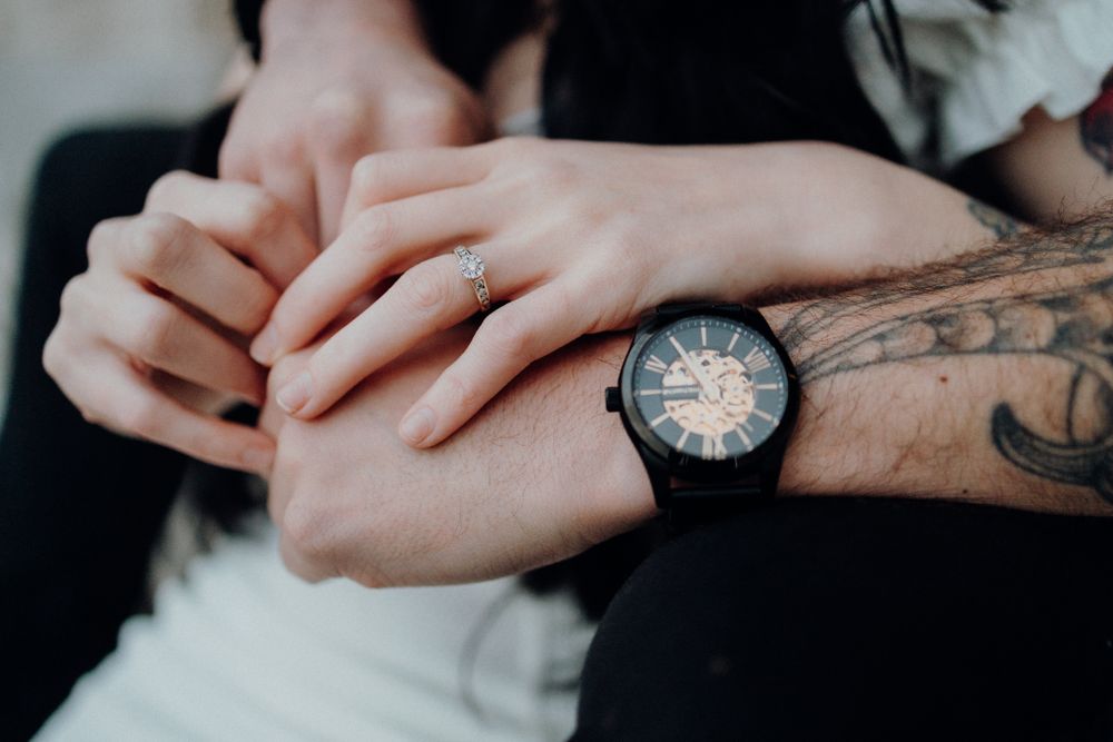 Close-up of hands with tattoos and a black watch against dark clothing.