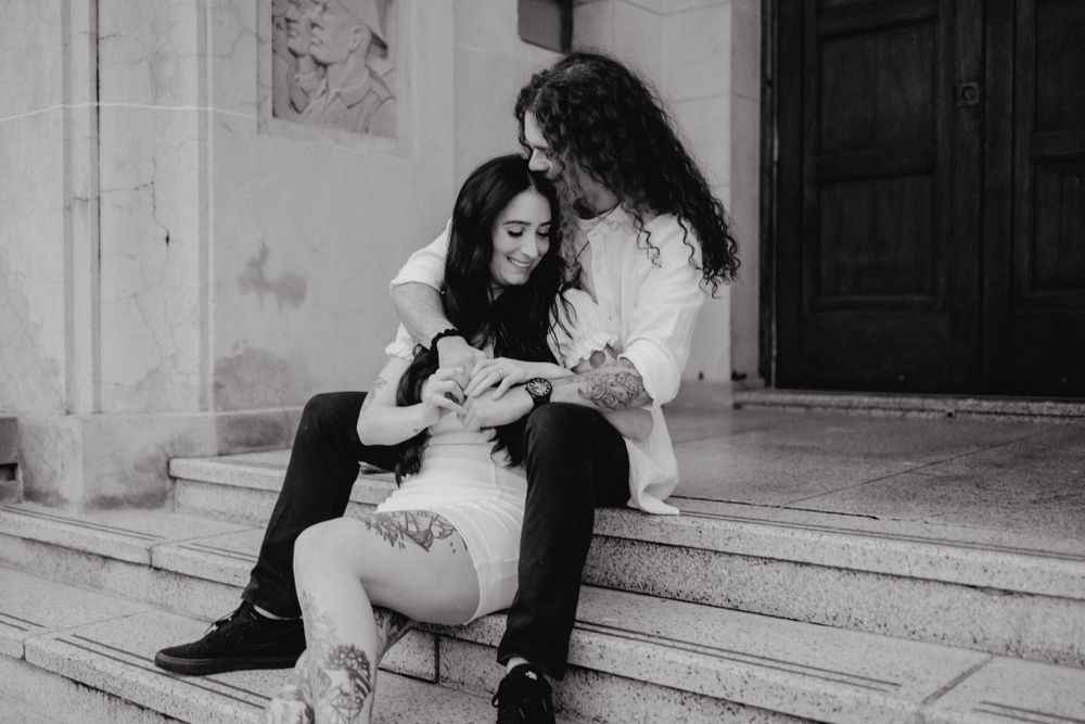 Two people sit close together on stone steps while looking at something between them.