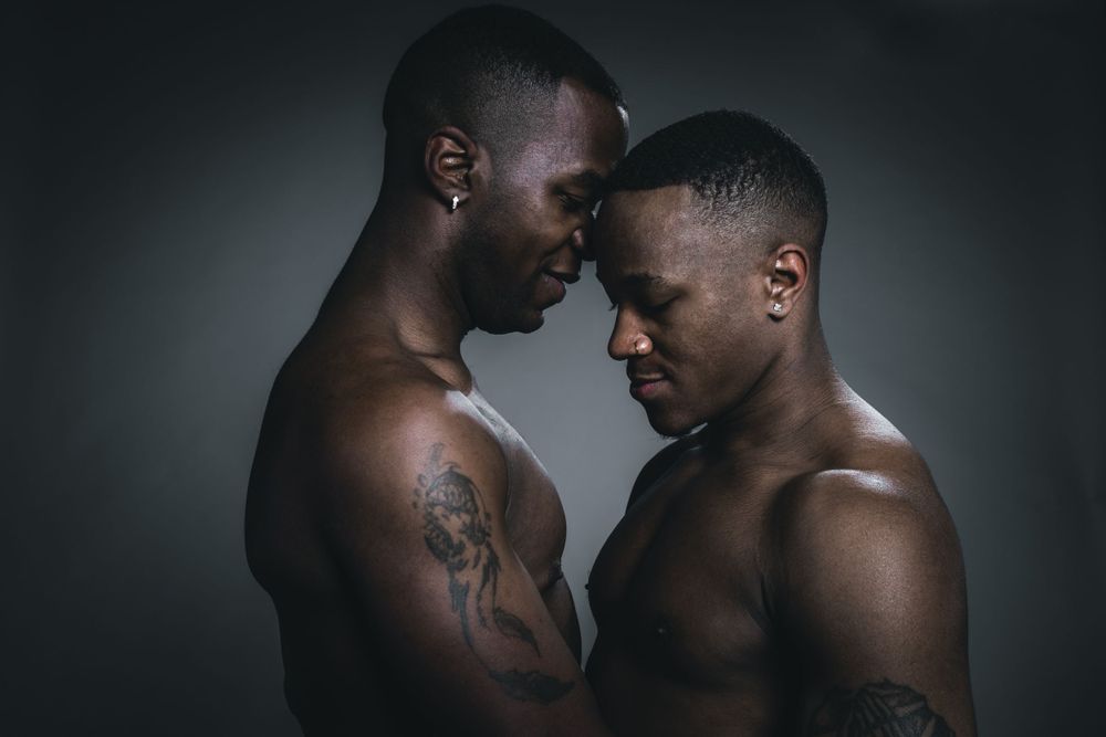 Two people in an intimate pose against a dark background, creating a striking artistic portrait.