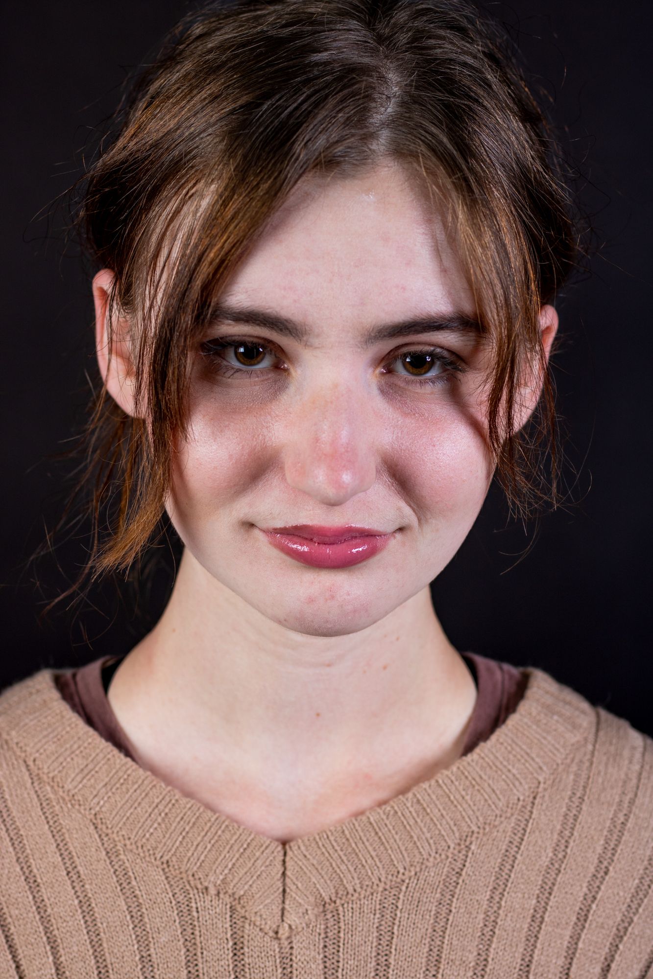 Studio portrait against black background showing soft natural makeup look.