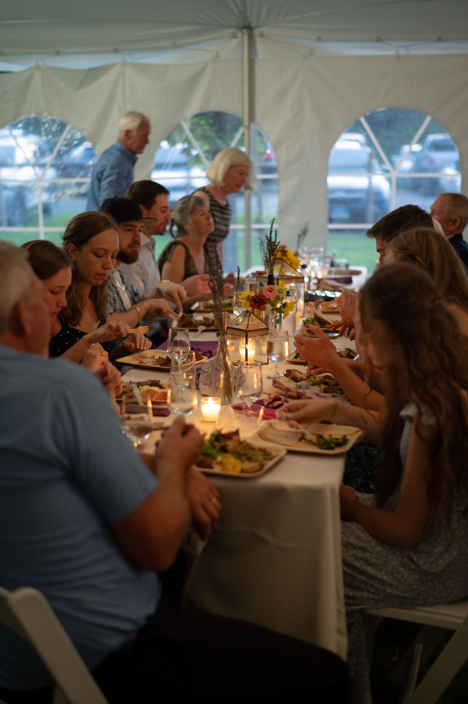 Wedding reception dinner under a white tent with guests enjoying a candlelit meal.
