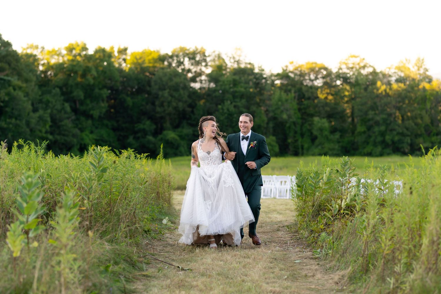 Couple walking together on rustic path through tall grass at sunset.