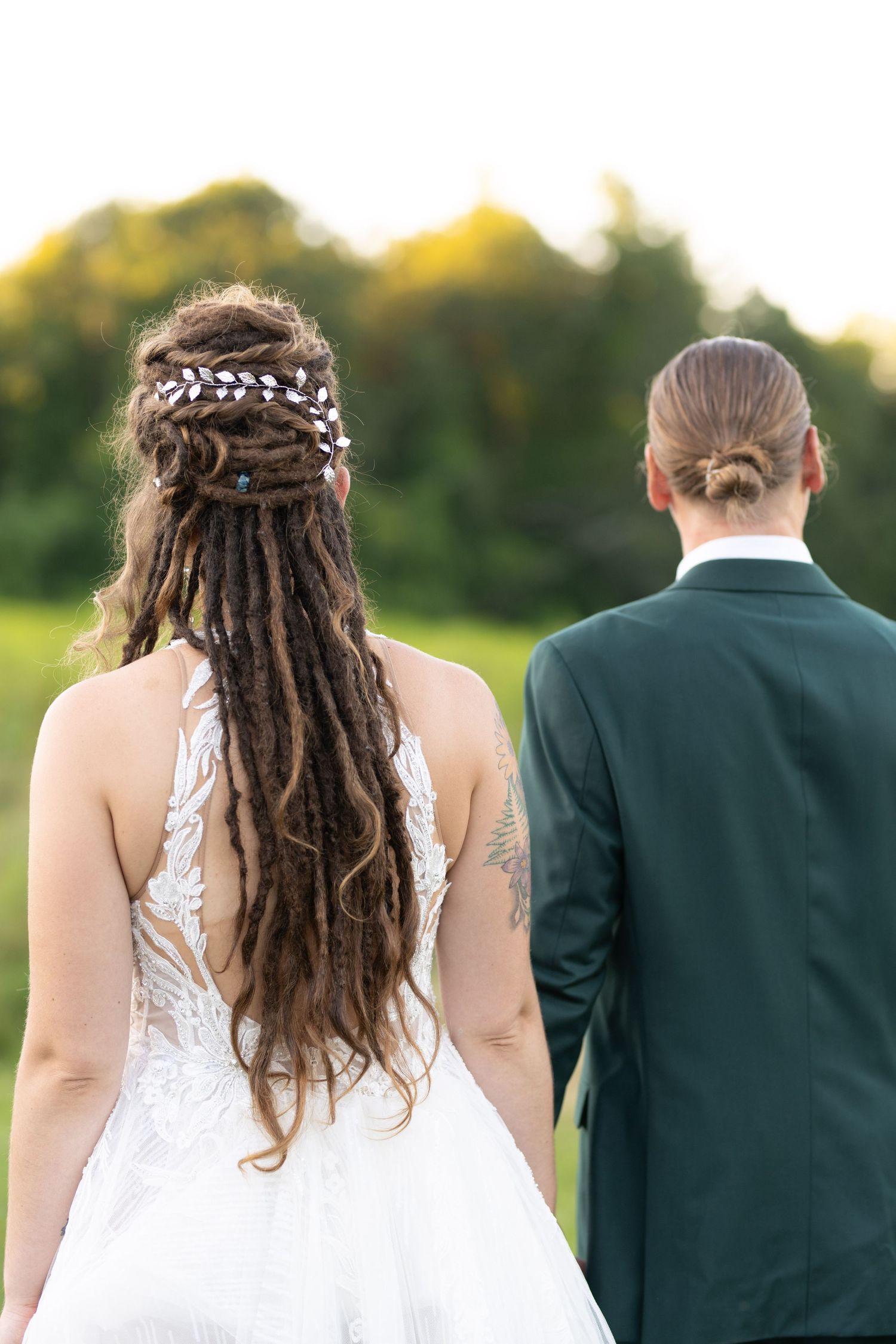Back view of newlyweds showing detailed lace dress and emerald suit against natural backdrop.