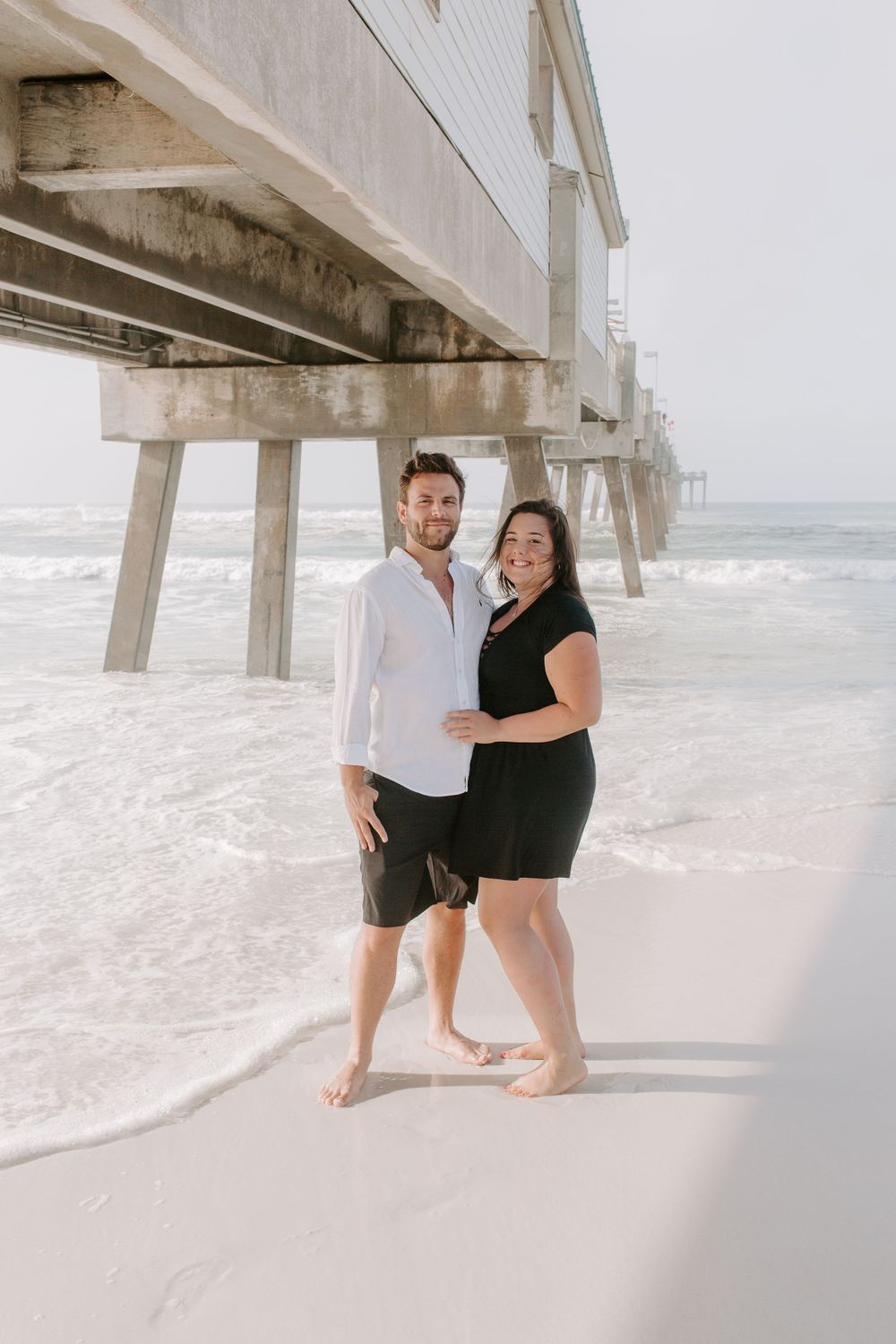 couple standing in front of a pier during their sunrise couples session