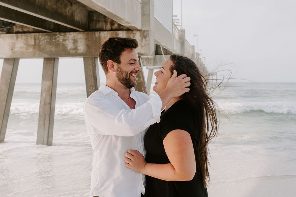 man pushing woman's hair back behind her ear during windy morning sunrise session