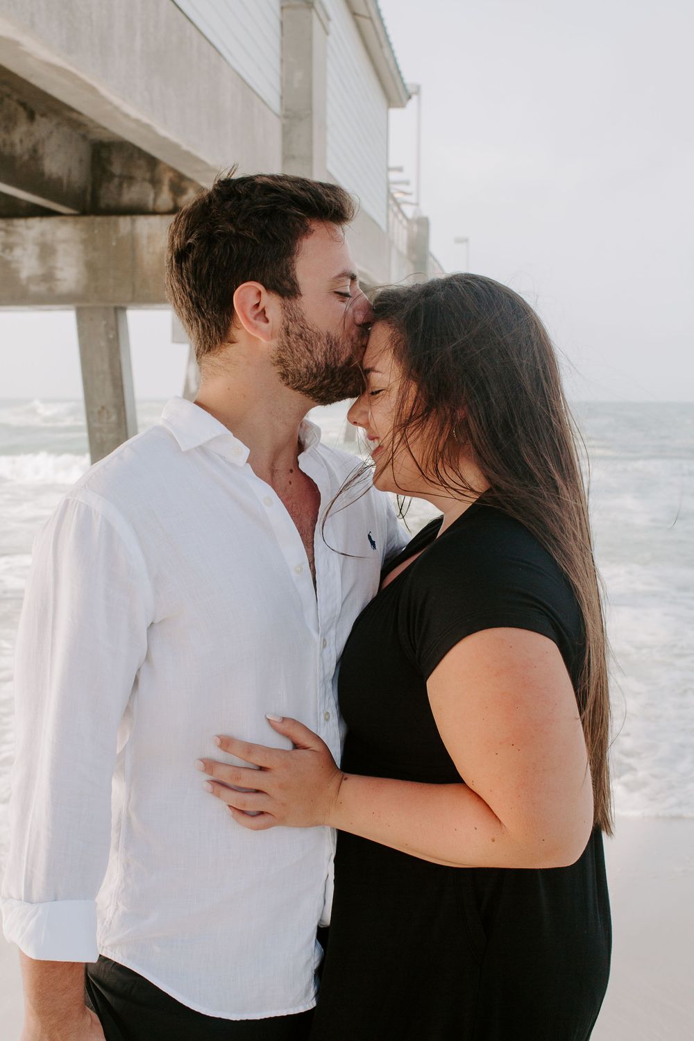 man kissing woman on the forehead during their sunrise beach session
