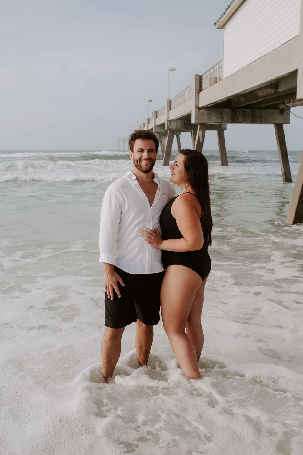 couple standing in the ocean in front of a pier along 30A