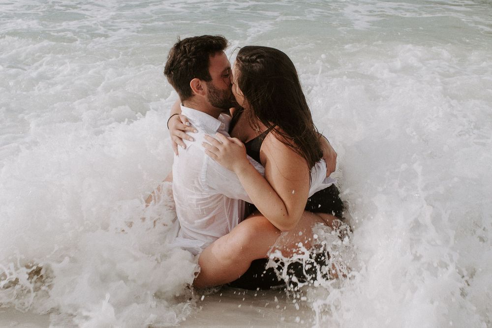 couple sitting in the water getting hit by it in Destin, Florida