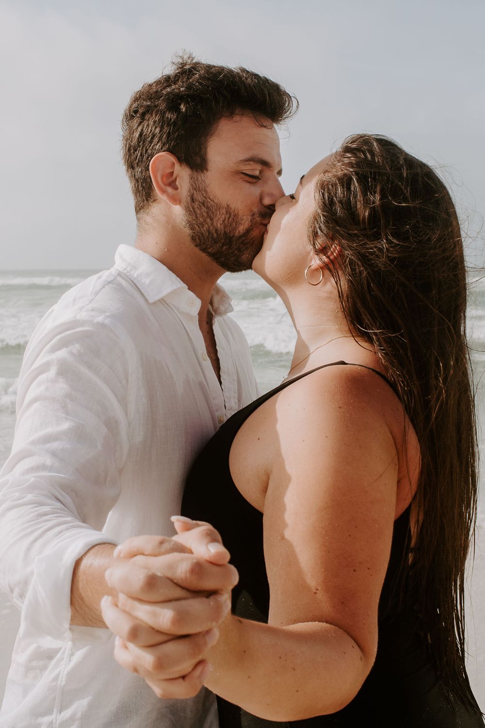 couple holding hands and kissing in front of the ocean on okaloasa island