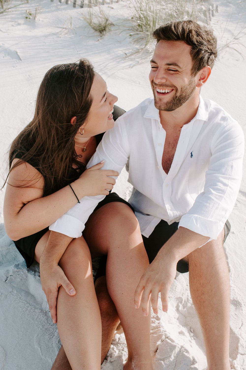 couple sitting in the sand on Okaloosa Island laughing at each during their sunrise session