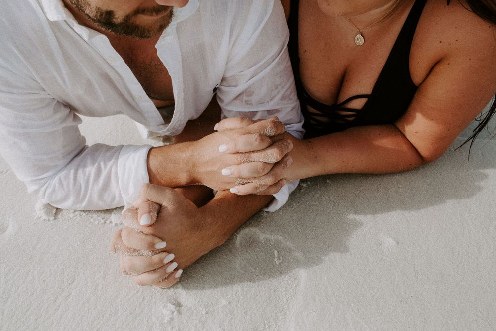 couple holding hands laying on the beach during their couple session in Destin, Florida