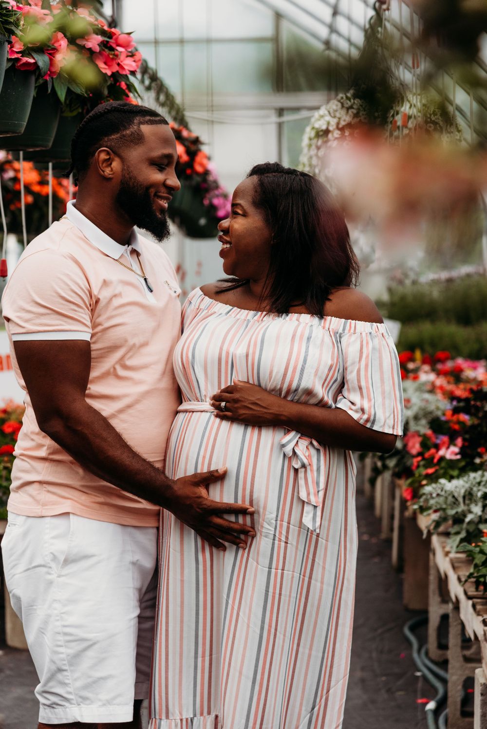 A joyful couple embraces among greenhouse flowers during a maternity photoshoot.