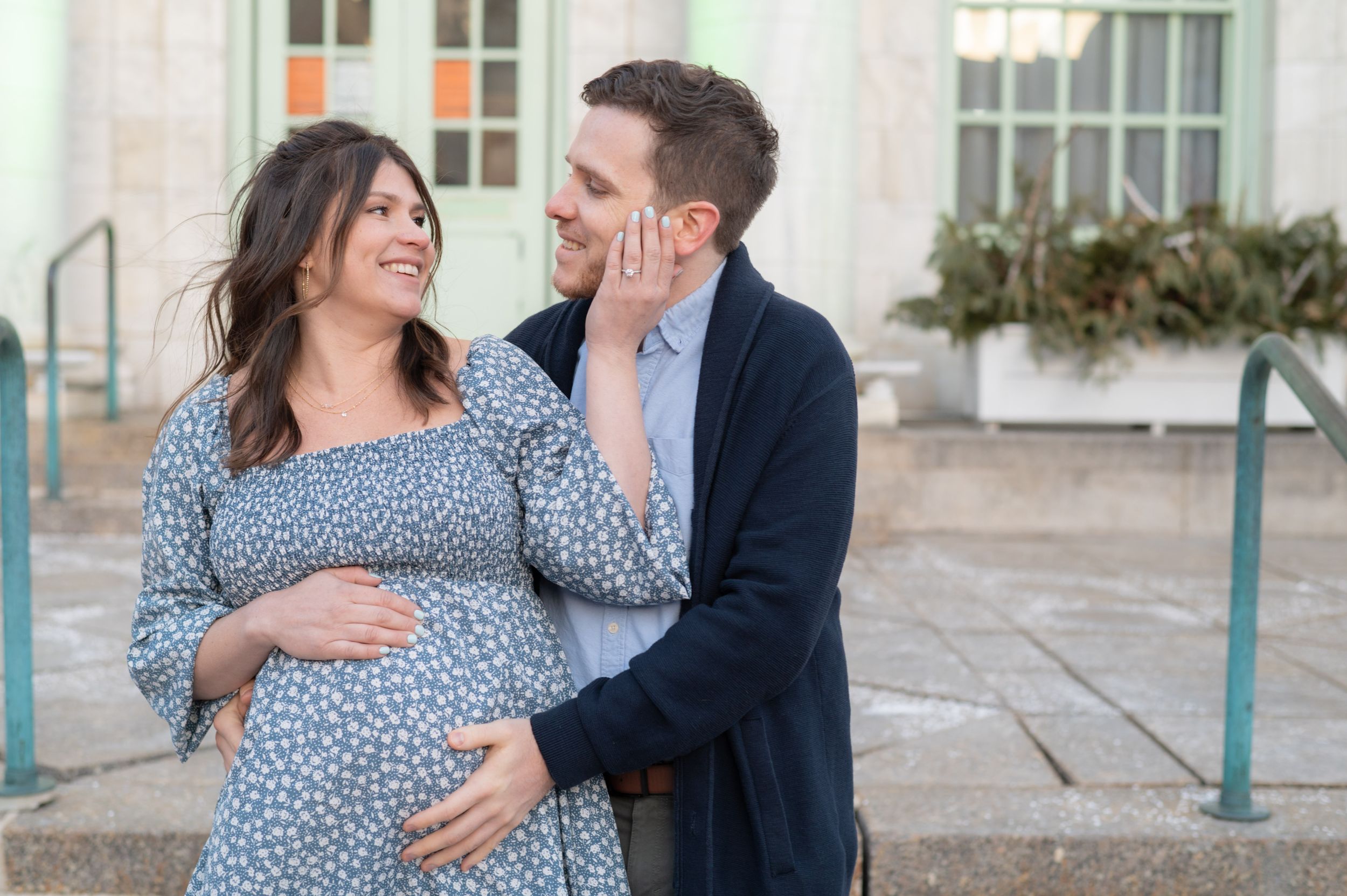 Sweet moment shared between expecting couple in front of classic architecture.