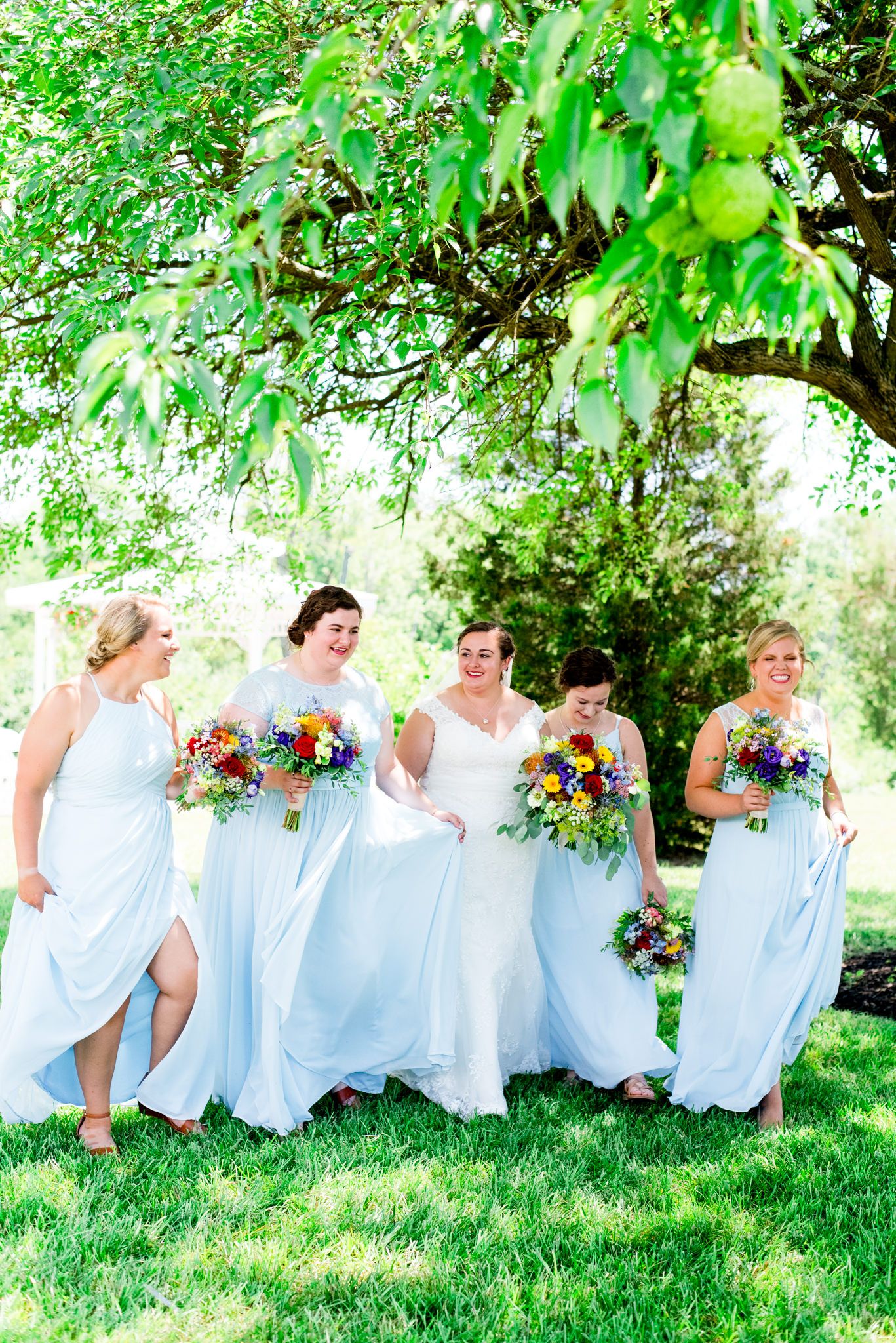 bridesmaids in light blue dresses walk under trees for a colorful outdoor summer wedding in Chicago