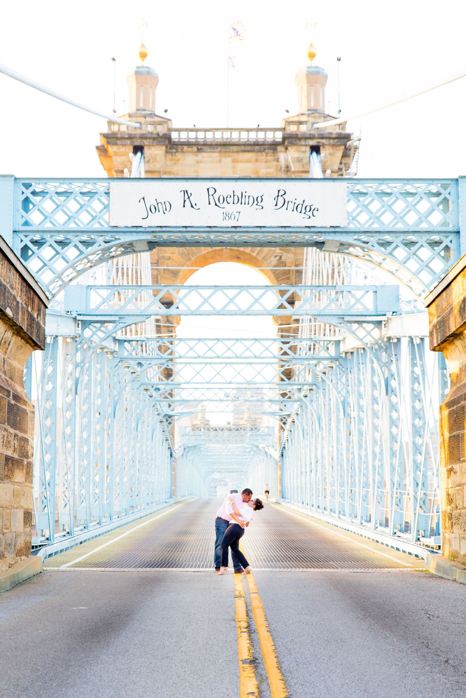 engaged couple kissing and dipping in the middle of blue Cincinnati Roebling Bridge