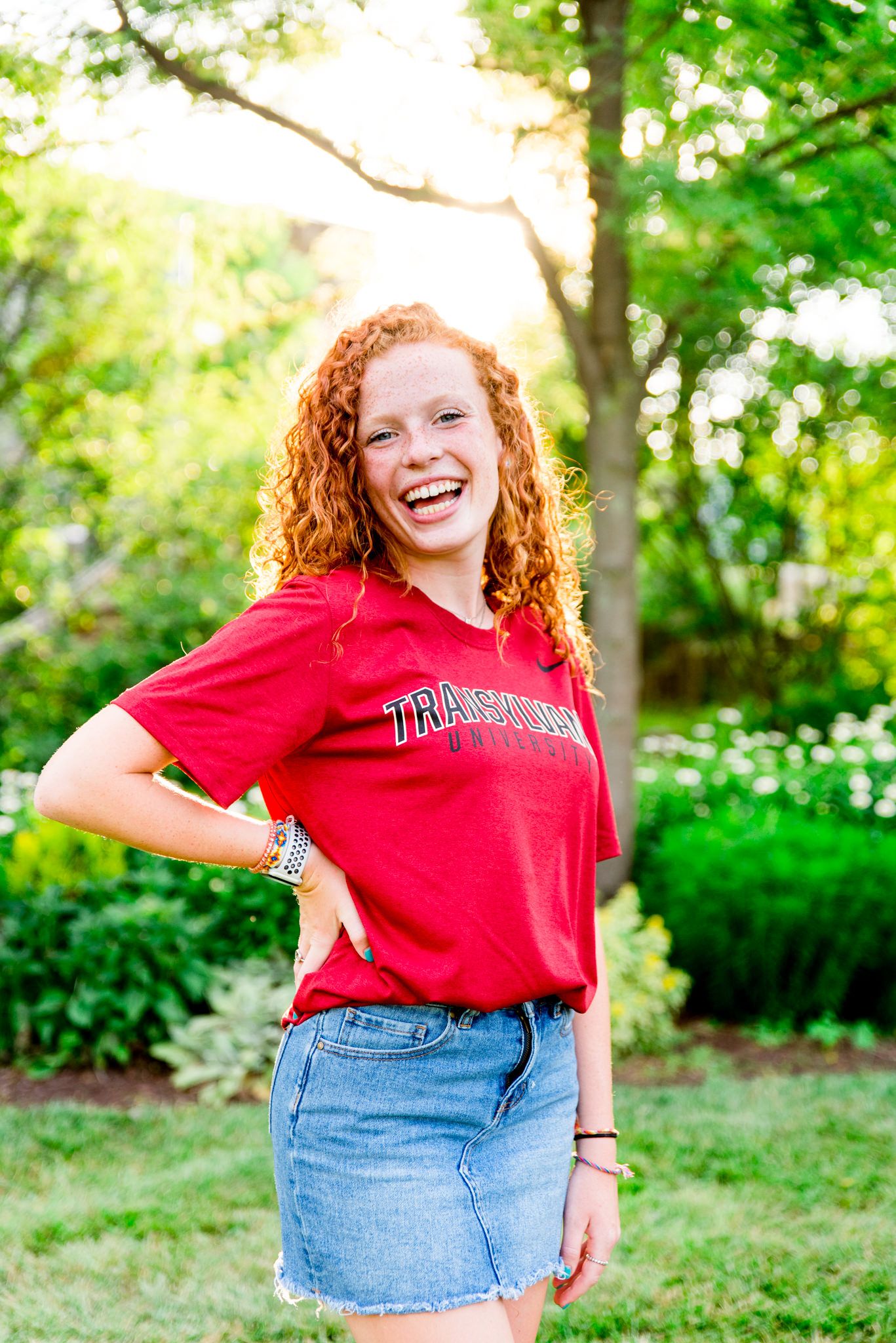 young woman in red Transylvania shirt taking senior pictures at Smale Park in front of trees at sunset