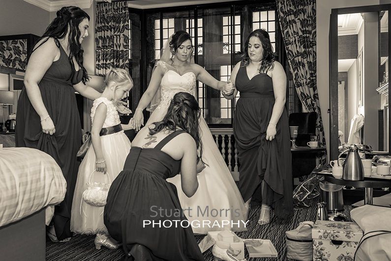 the bridesmaids work on th bride in her wedding dress getting her ready to get married