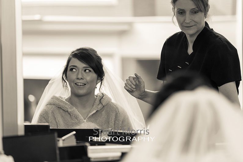 bride looks off to the side reflected in the mirror as she gets her hair and makeup done
