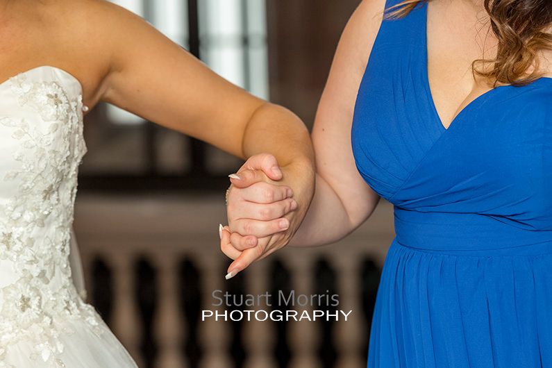 the bride gets a helping hand from a bridesmaid steadying her as she gets help putting her shoes on