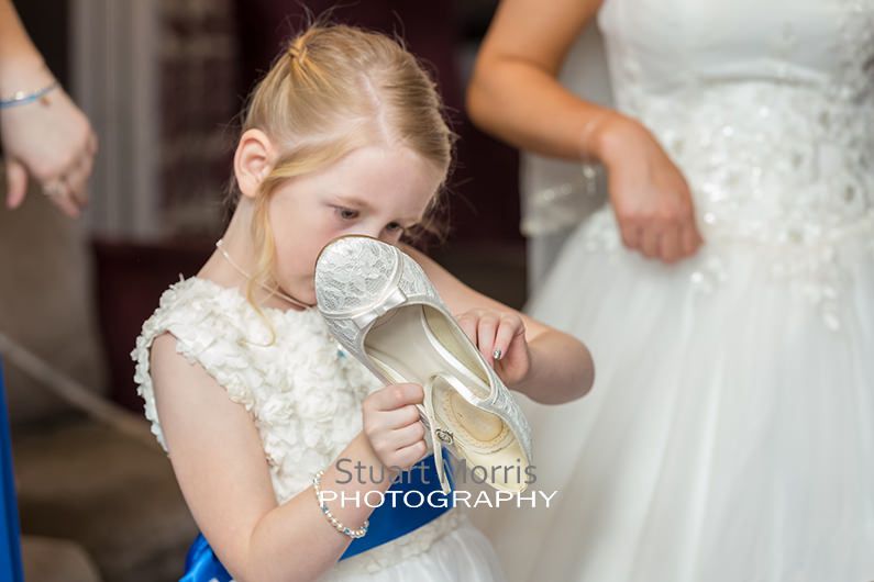flower girl picks a label off the bottom of the brides shoe during the prep at abbey house barrow in furness