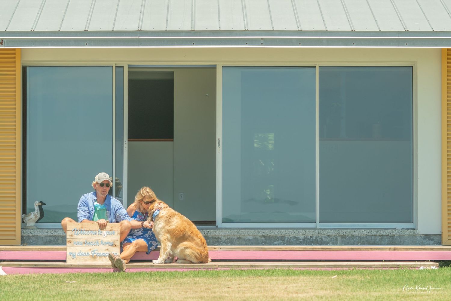Modern beach house exterior with people and dog relaxing on steps.