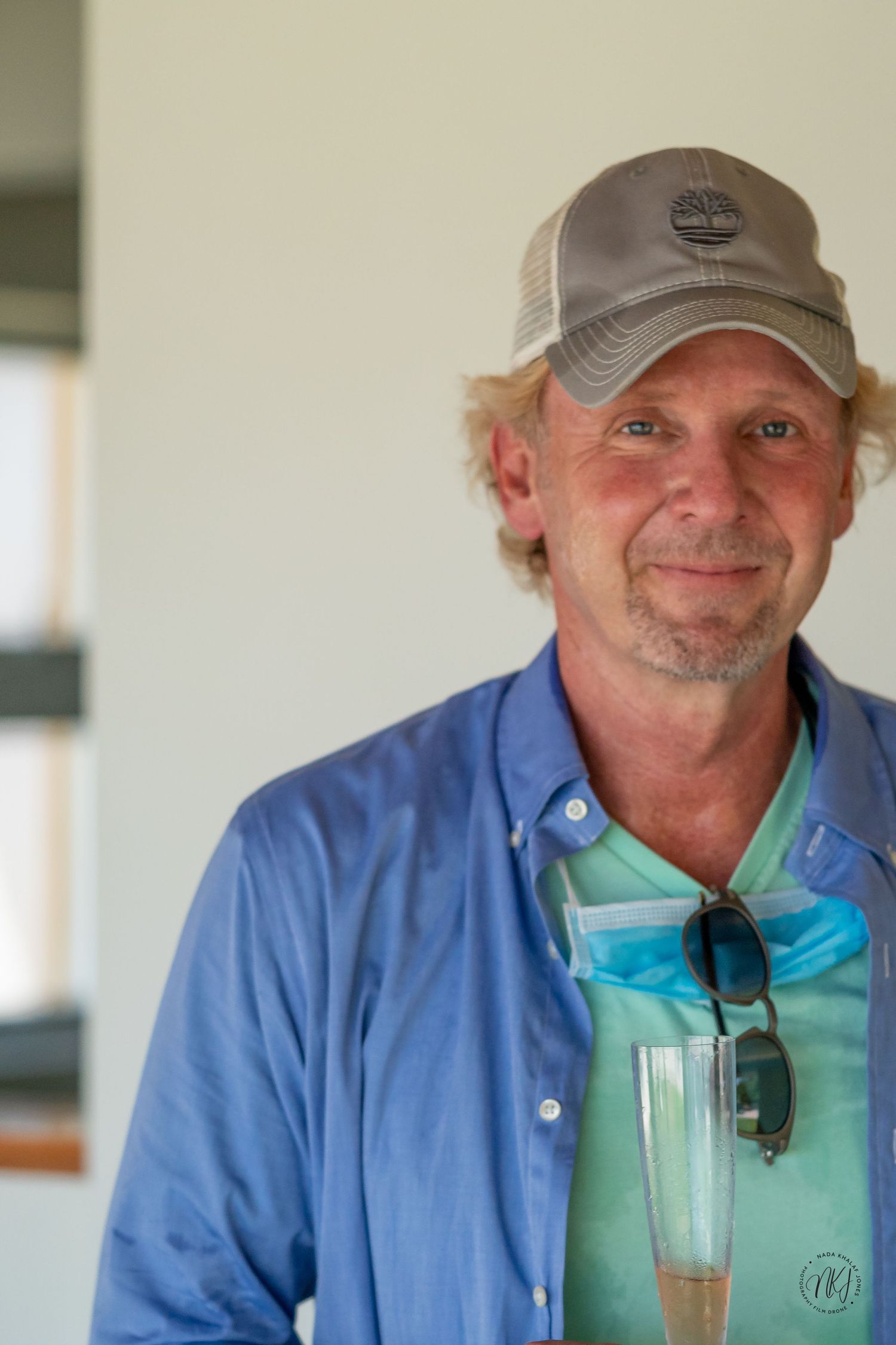 Portrait of person wearing blue shirt and baseball cap against white wall.