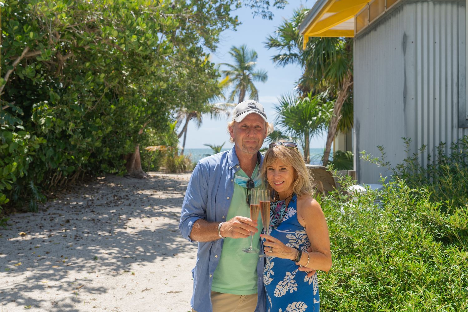 Couple embracing on tropical path with palm trees and greenery.