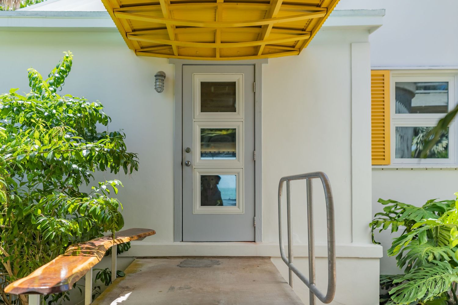 Modern white house entrance with yellow awning and potted plants on a covered porch.
