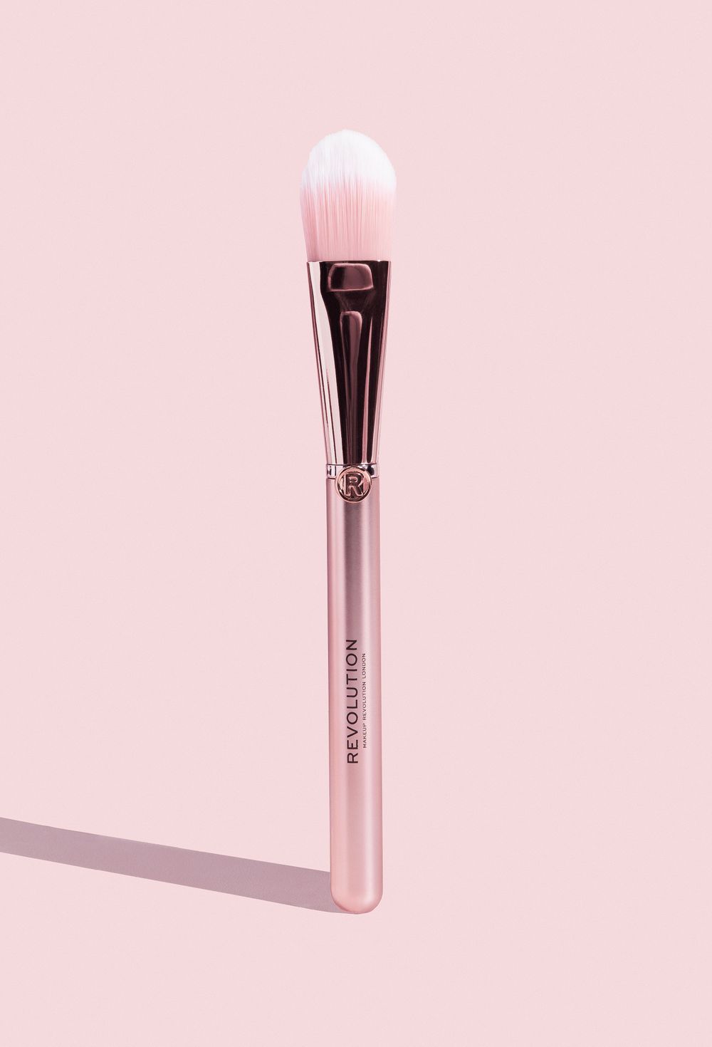 Elegant rose gold makeup brush photographed against soft pink background.