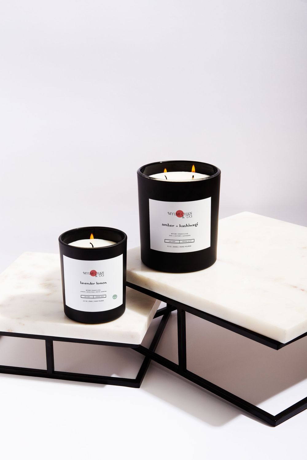 Two black scented candles arranged on white books with modern styling.