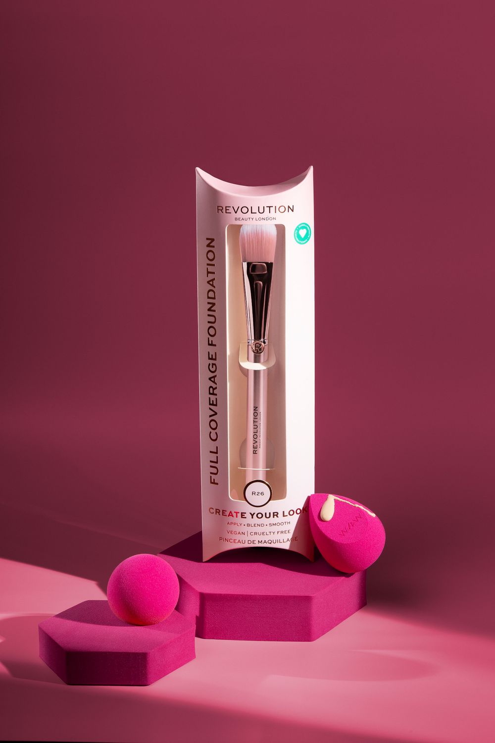 Revolution makeup brush packaging with pink beauty sponges on burgundy background.