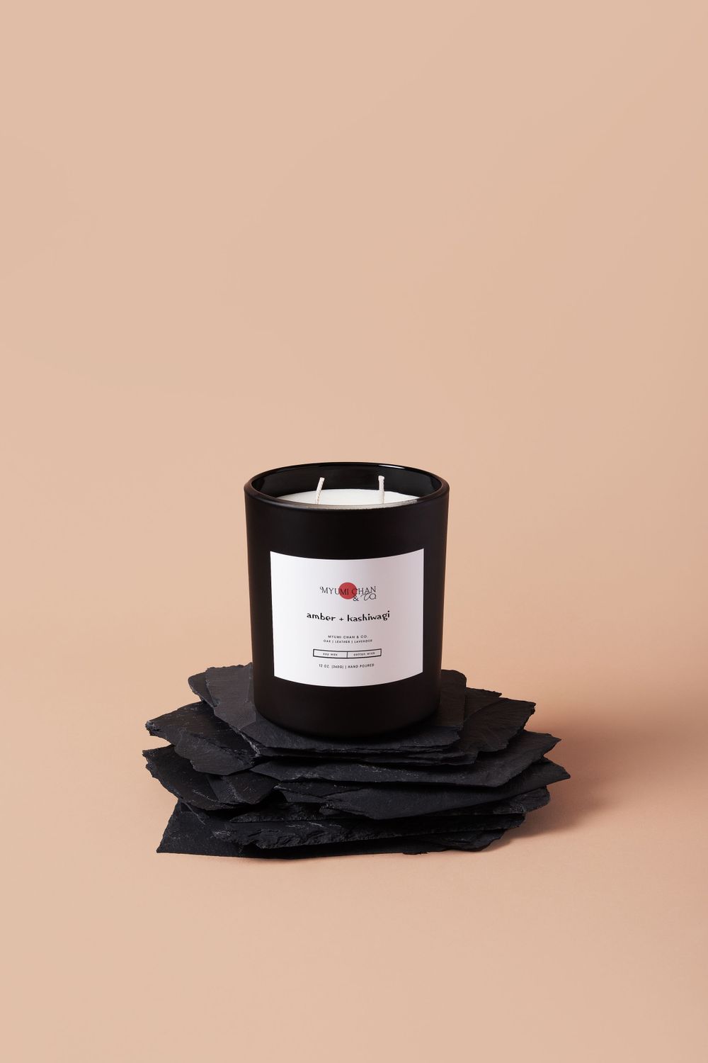 Black scented candle displayed on layered black stone coasters against beige background.