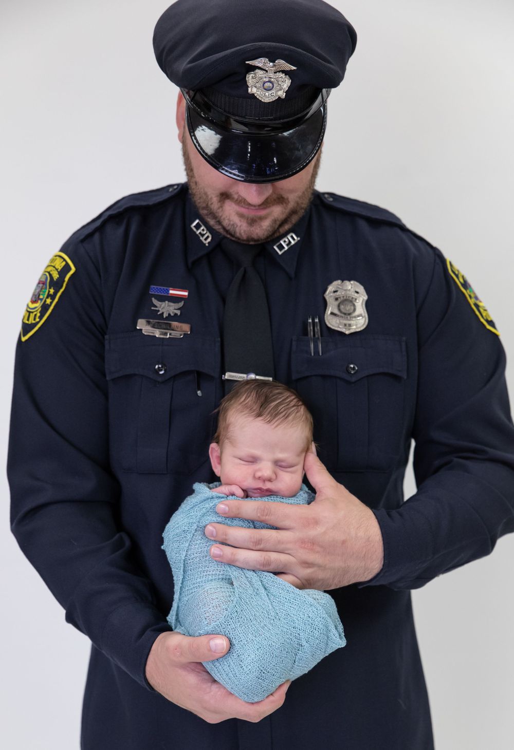 Newborn photography of sleeping baby held by father in police uniform
