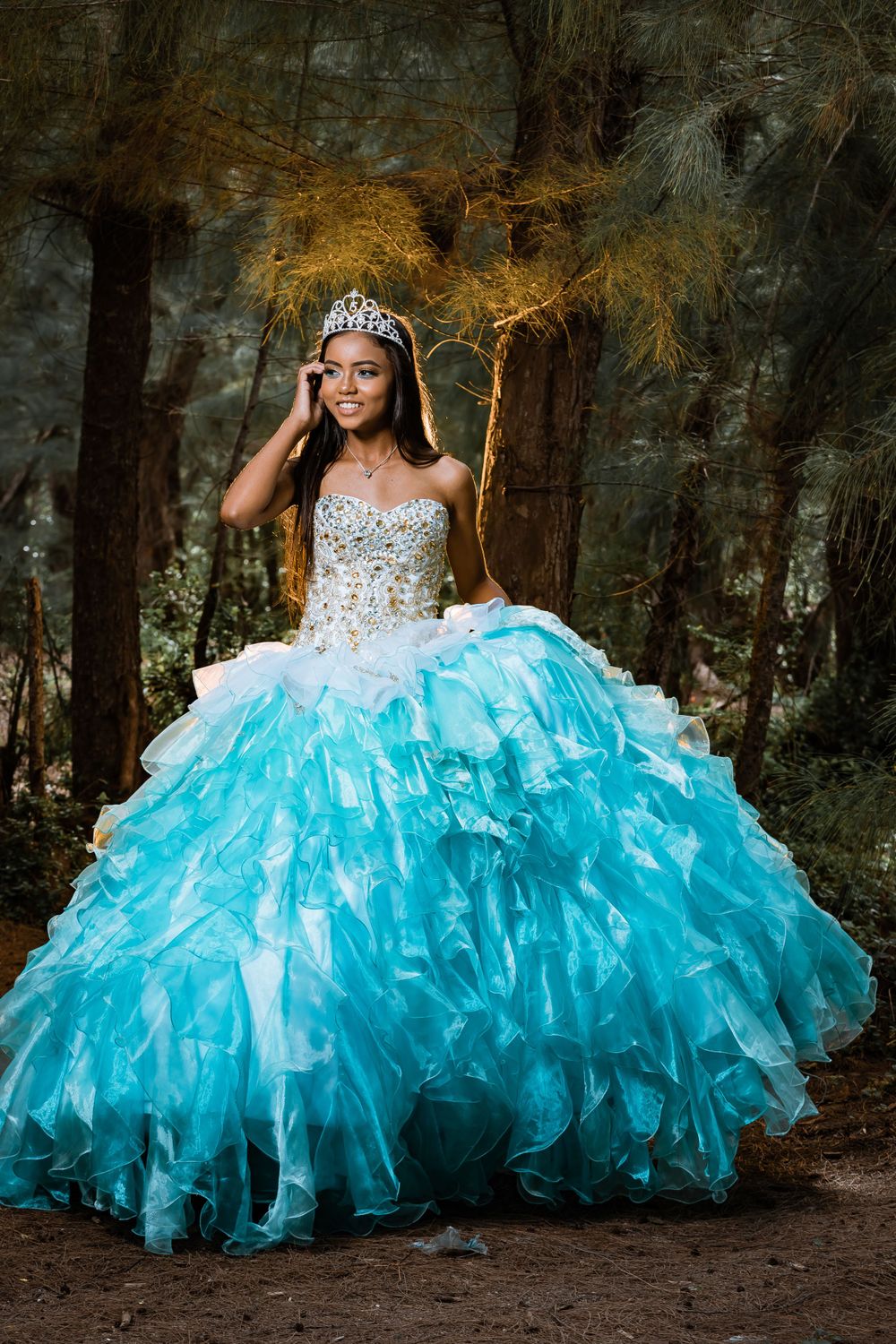 A stunning turquoise quinceañera dress photographed in a moody forest setting.