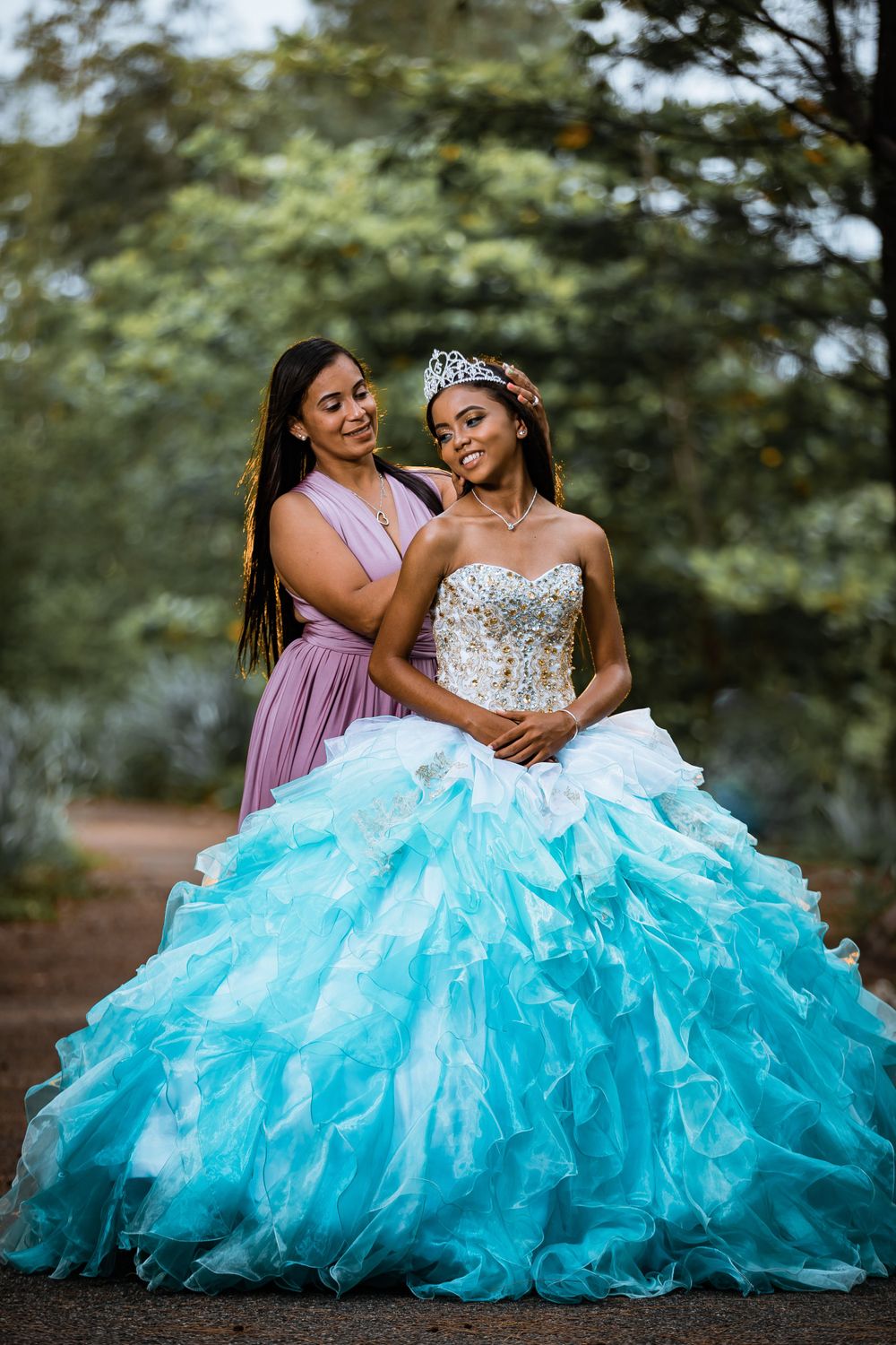 A stunning turquoise quinceanera ball gown with ruffled layers and sparkly bodice paired with a tiara and purple bridesmaid dress.