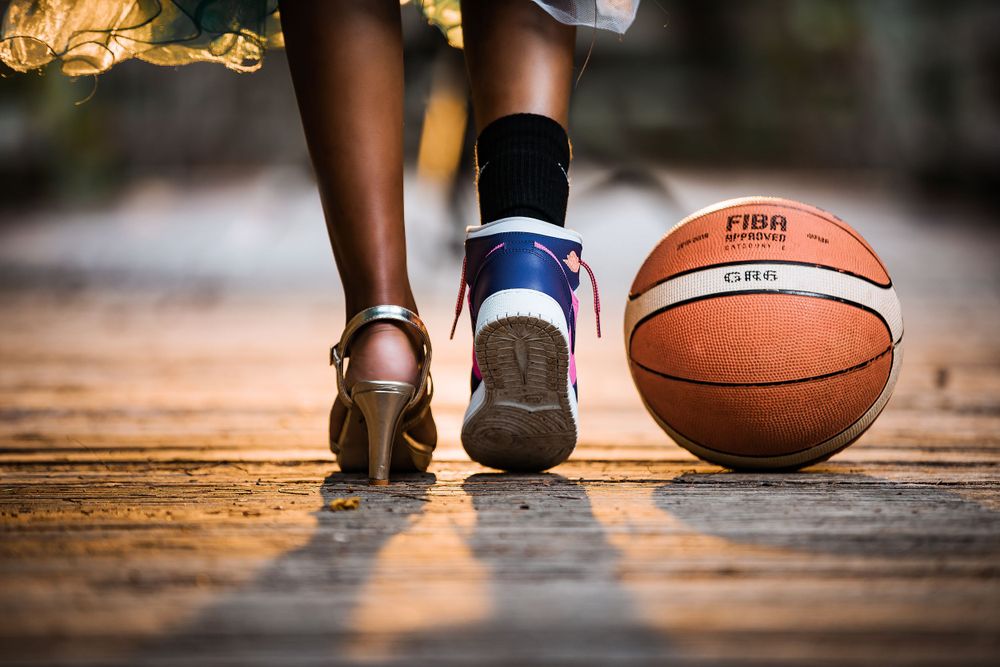 Close-up shot of basketball shoes and a FIBA regulation basketball on a wooden court.