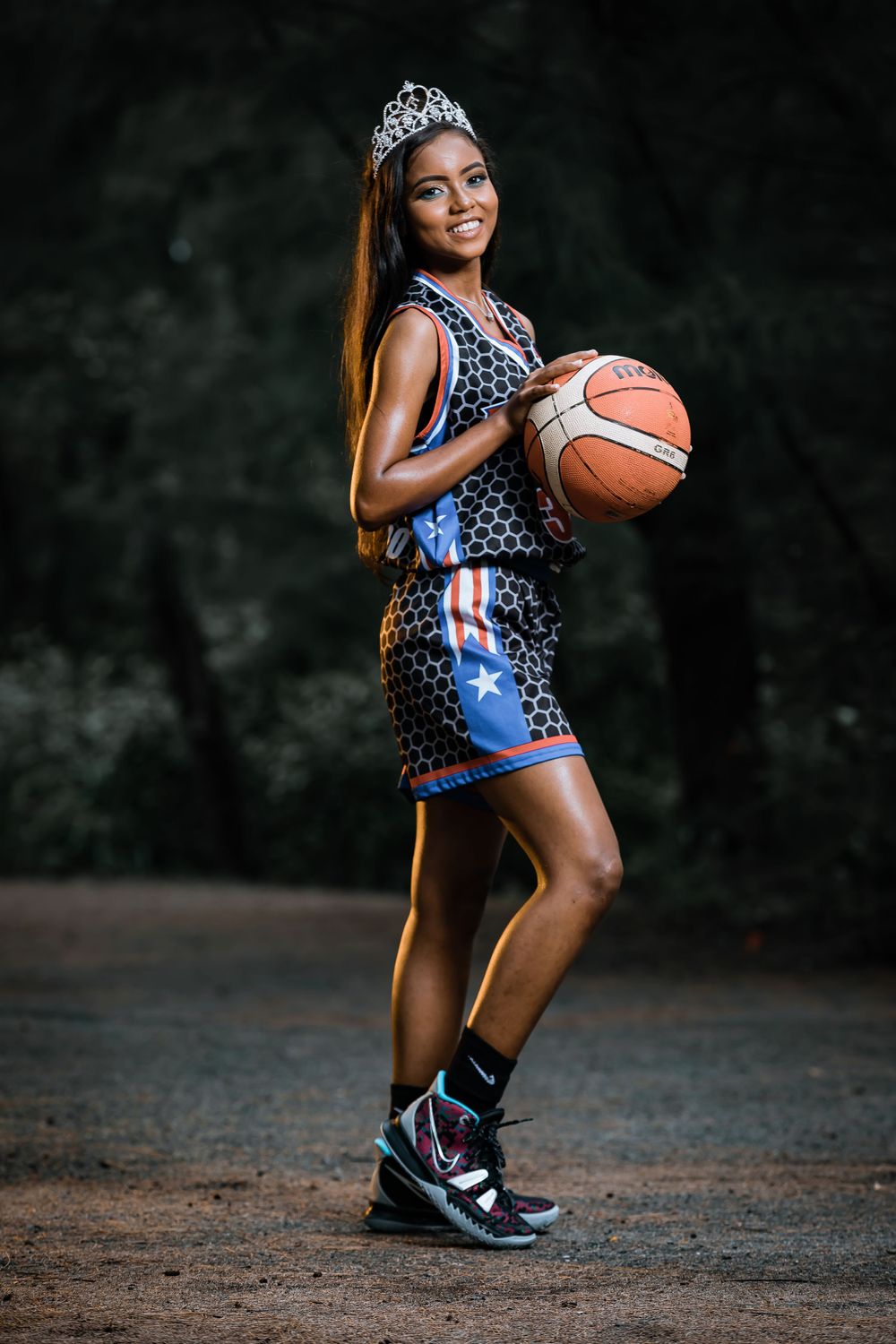 Athletic portrait featuring basketball uniform and tiara against dark outdoor background.