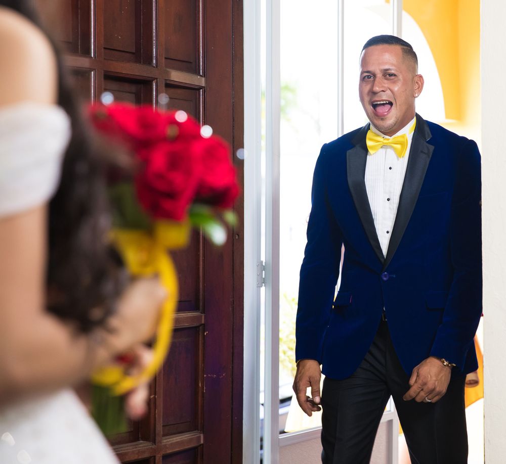 First look wedding moment captured through doorway with red and yellow bouquet.
