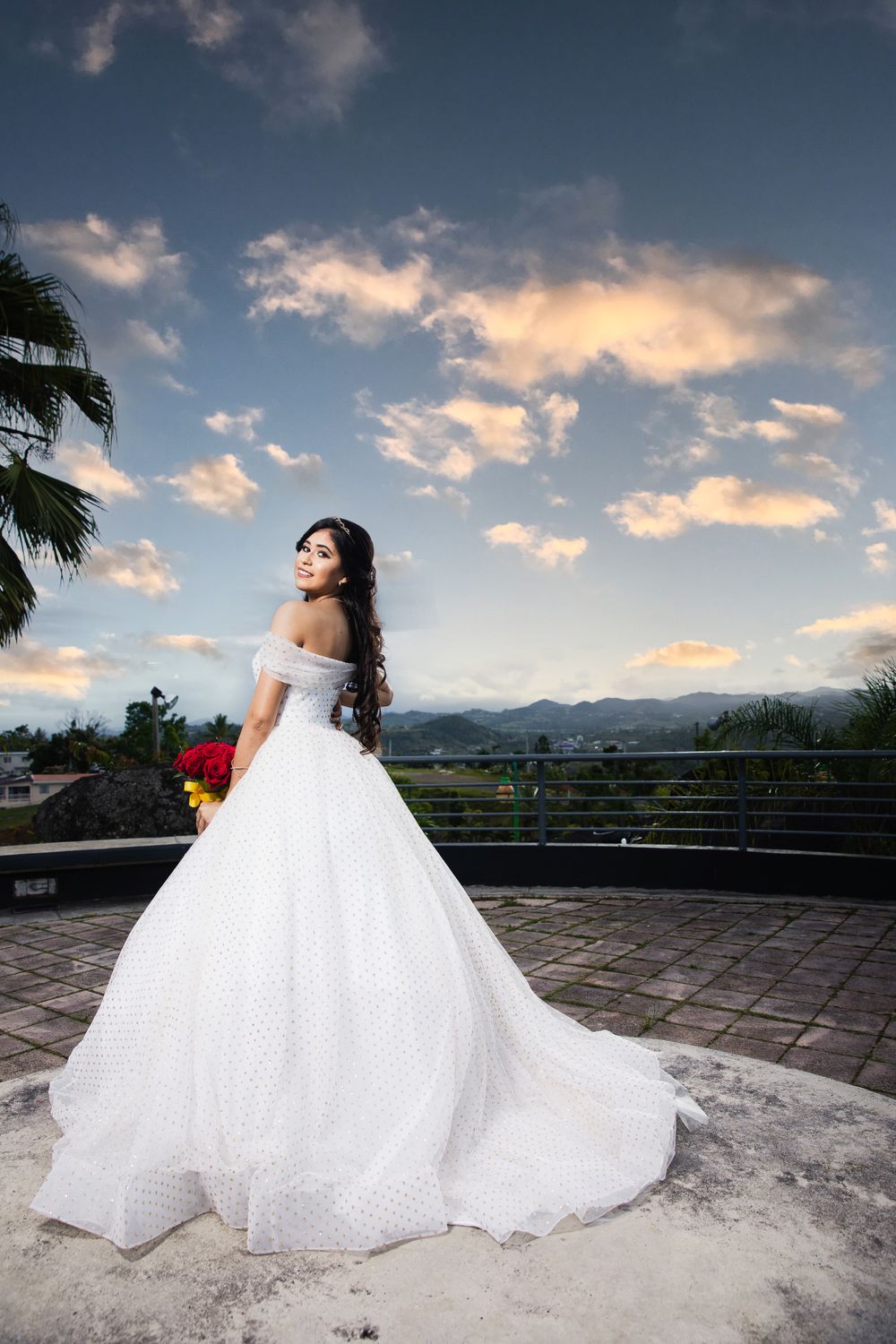 Dramatic bridal portrait in white ball gown against sunset mountain landscape.