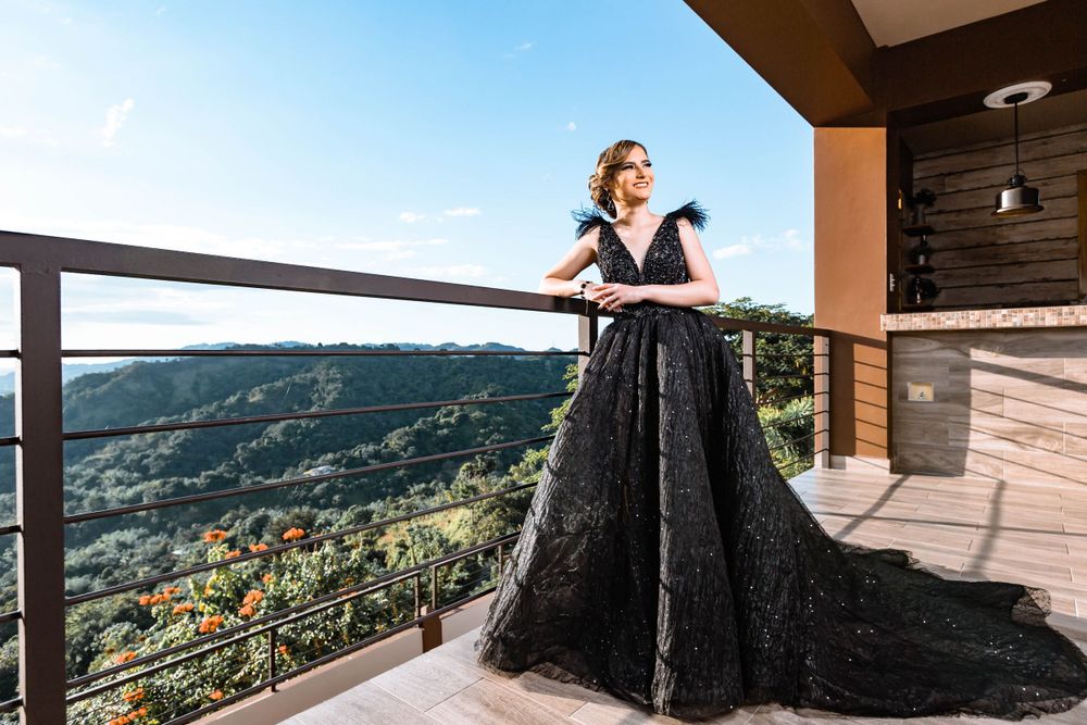 A dramatic black ball gown against a mountain backdrop on a luxury balcony at sunset.