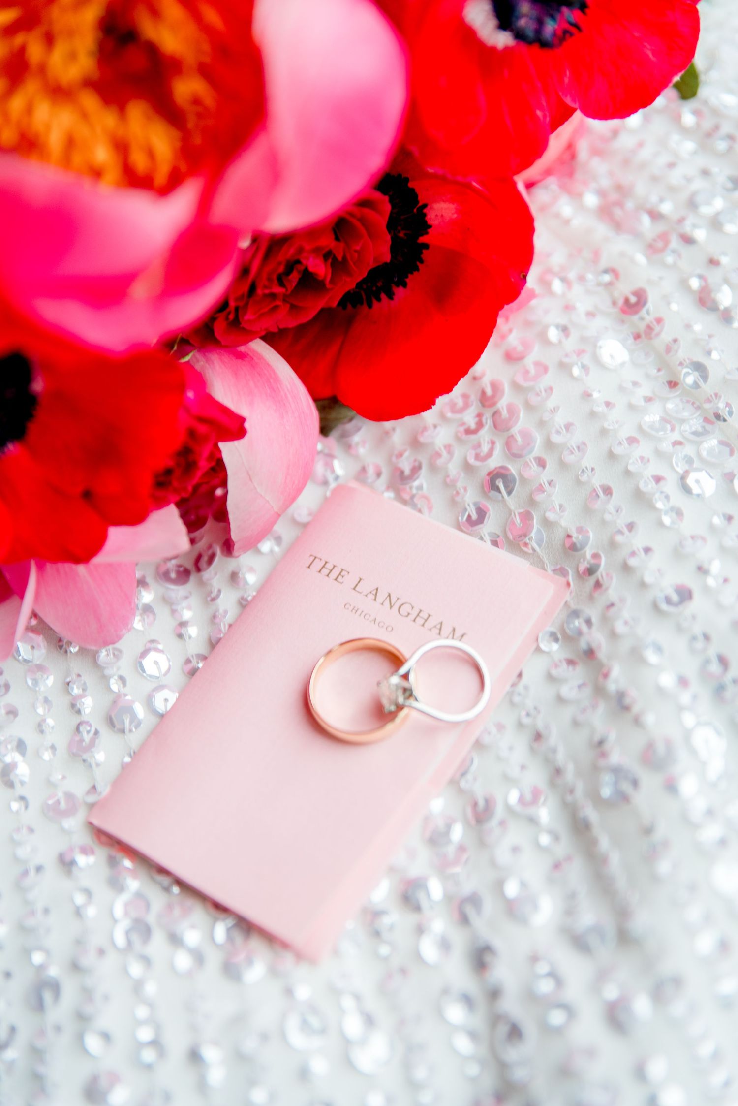wedding bands on Langham key card with red flowers and sequin dress