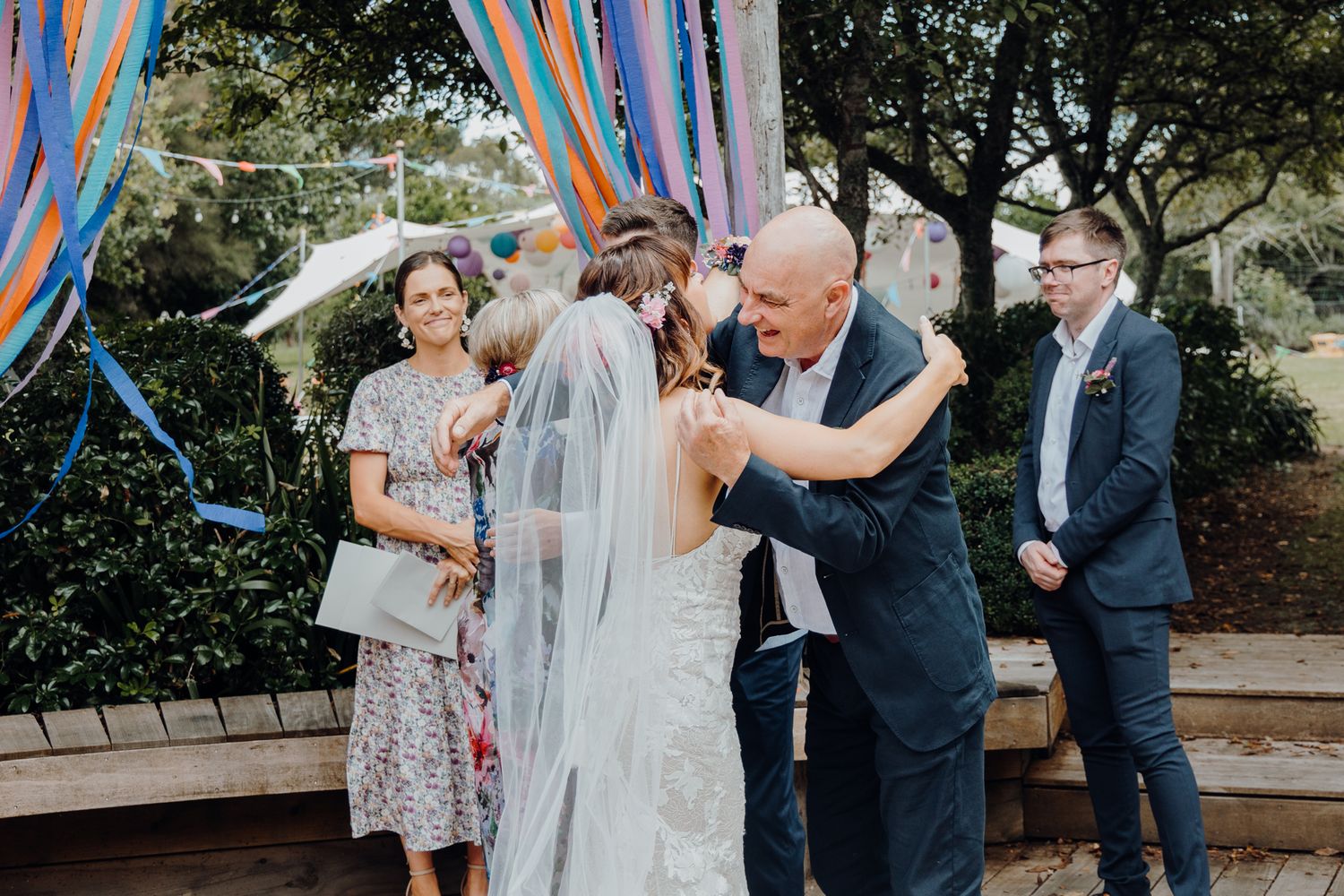 Emotional moment during outdoor wedding ceremony with blue and orange streamers in background.
