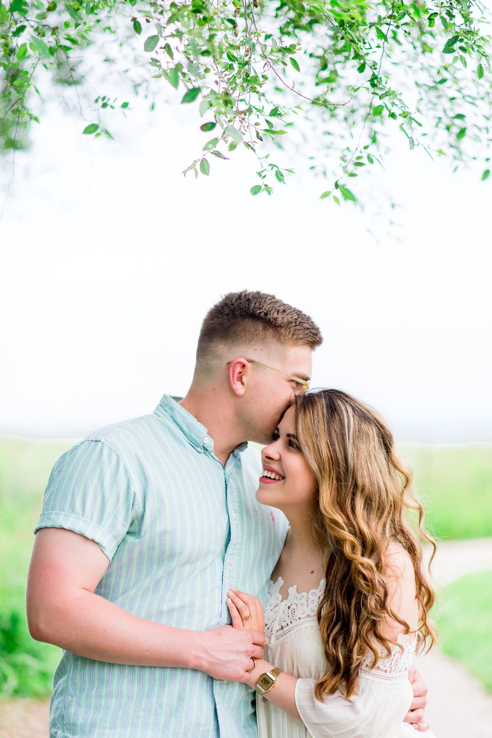 young man whispers in ear of his fiancee as she laughs and smiles at Montrose Harbor Chicago sunrise engagement pictures
