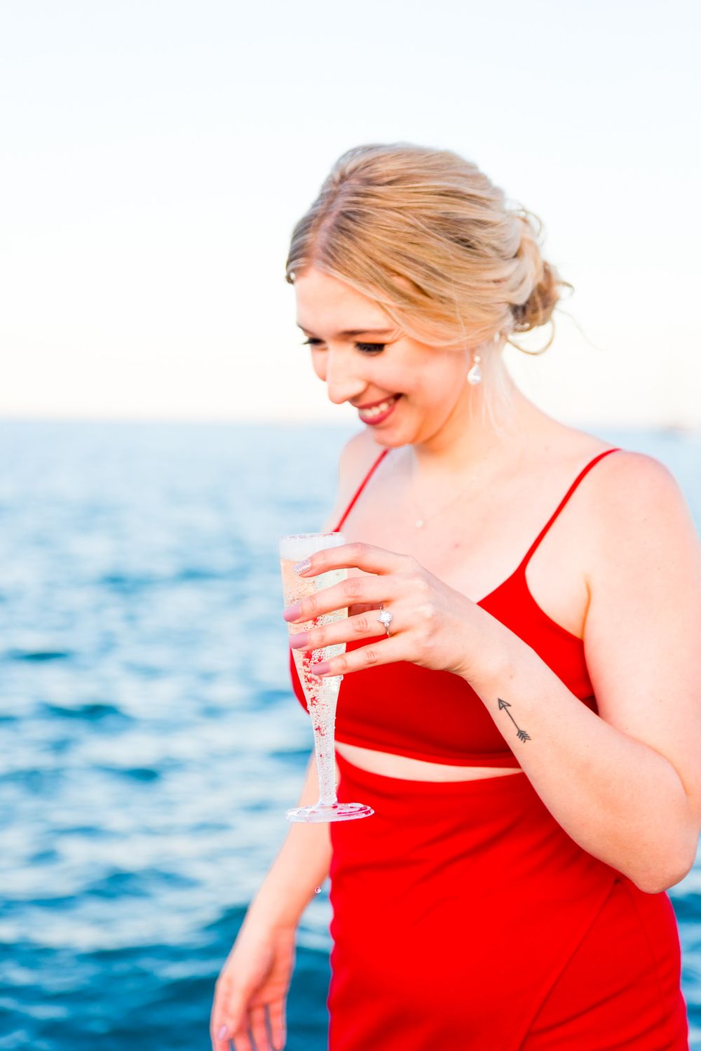 woman in red dress holding glass of champagne and smiling next to Lake Michigan on Chicago lakefront trail at sunset