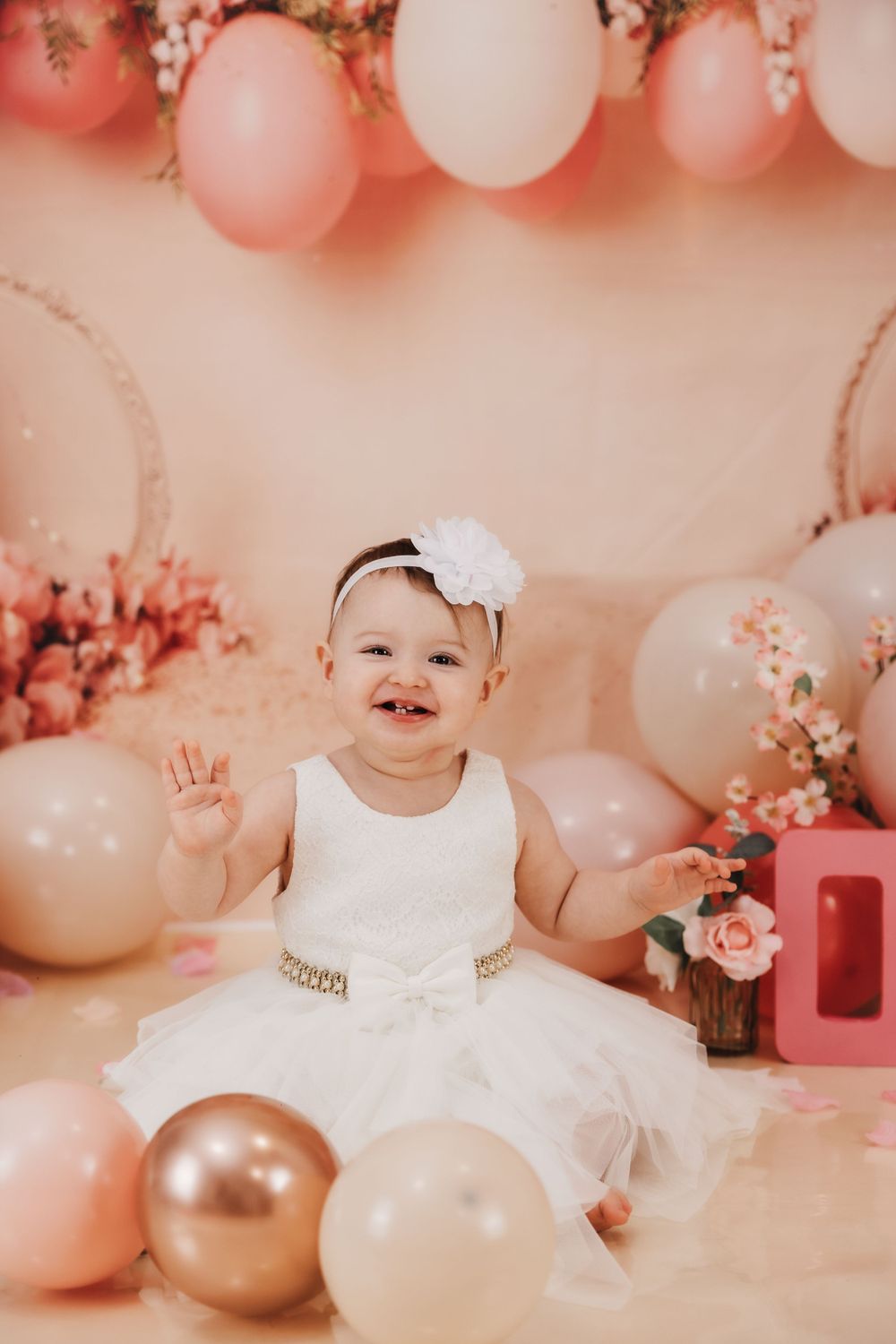 Elegant first birthday photoshoot with pink balloons, roses, and white tulle dress.