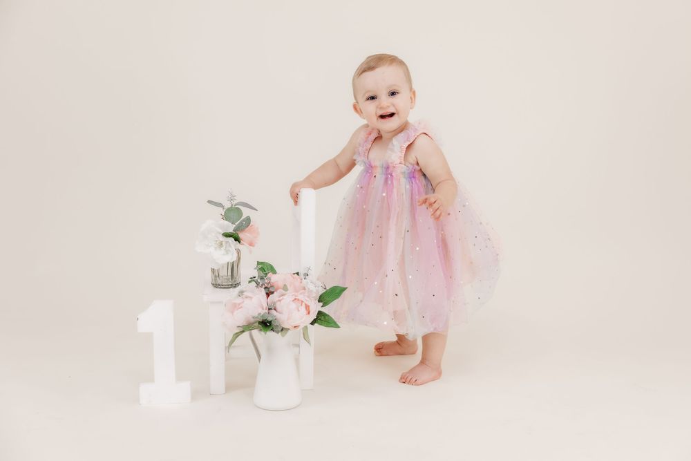 First birthday setup with pink tulle dress, white decorations, and floral arrangements.