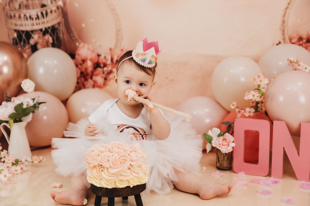Cake smash session with white tulle dress and pink frosted cake on black stand.