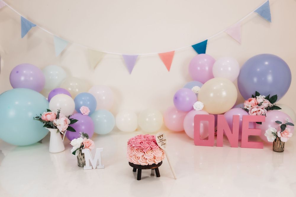Whimsical birthday scene with pastel balloons, bunting flags, and pink decorative elements.