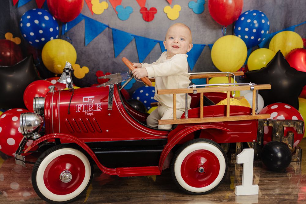 Vintage themed first birthday photo with red pedal fire truck and balloon decorations.